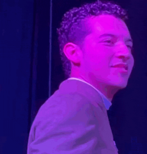 a man in a suit is standing in front of a purple light and smiling .