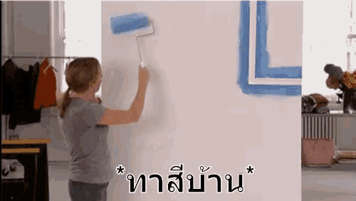 a woman is painting a wall with a paint roller in a room .