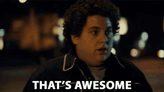 a man with curly hair says " that 's awesome " in front of a blurry background