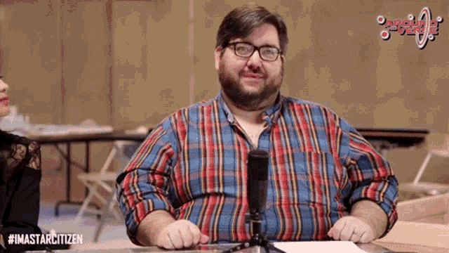 a man in a plaid shirt is sitting in front of a microphone with the hashtag #imastarcitizen on the bottom