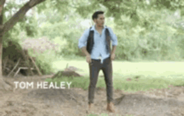a man in a blue shirt and brown pants is standing in a field with the name tom healey on the bottom right