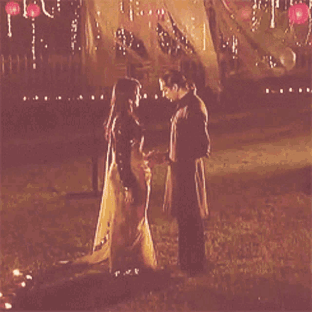 a man and a woman are standing in the grass looking at each other with lanterns in the background
