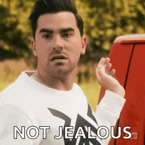 a man in a white shirt is standing next to a red van and says " not jealous "