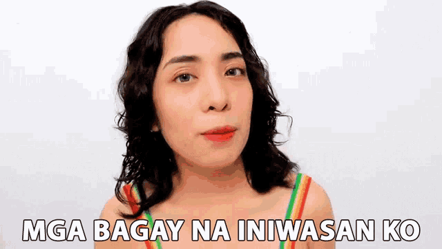 a woman in a rainbow tank top is making a funny face with the words mga bagay na iniwasan ko above her .