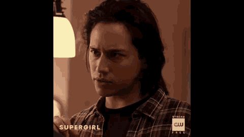 a man in a plaid shirt is standing in a room with a lamp .