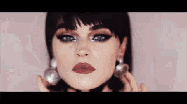 a woman with short black hair and bangs is wearing a white shirt and earrings .