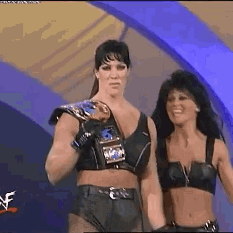 a couple of women standing next to each other on a stage . one of the women is wearing a wrestling belt .