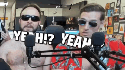 a man wearing sunglasses is talking into a microphone while another man holds up a sign that says yeah