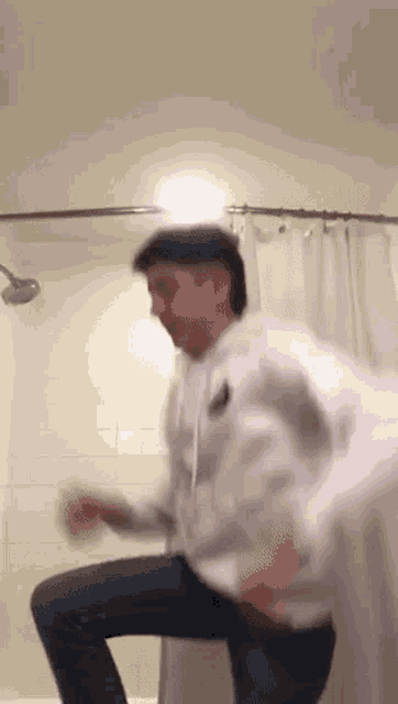 a man is dancing in a bathroom with a shower curtain behind him .