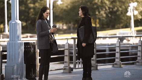 two women are standing next to each other on a sidewalk with nbc written on the pole