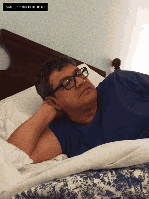 a man wearing glasses is laying in bed with a smile 17 on phhphoto sticker above him