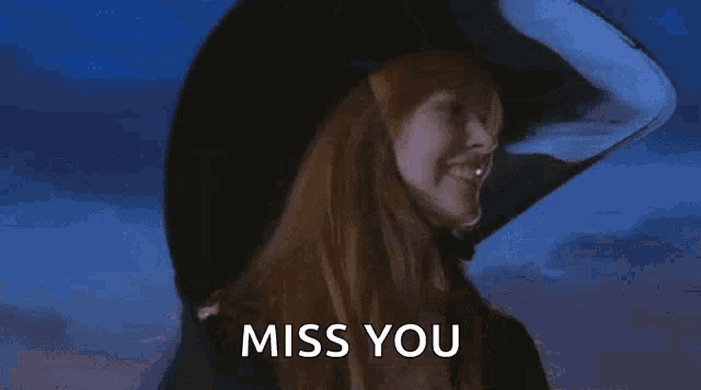a witch with red hair is wearing a large black hat and says miss you .