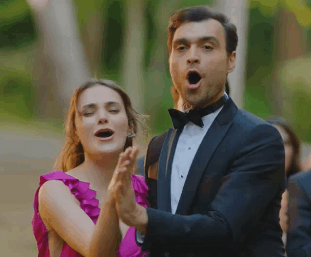 a man in a tuxedo and a woman in a pink dress are clapping together