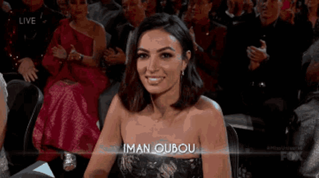 a woman in a strapless dress is sitting in a crowd with the name iman oubou