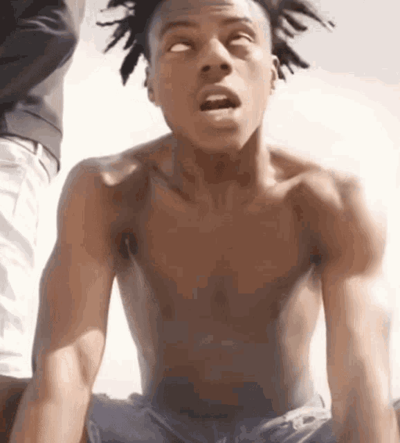a shirtless man with dreadlocks is sitting down