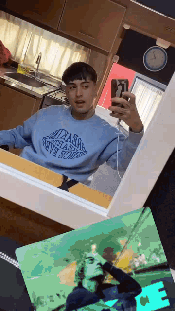 a man taking a selfie in front of a mirror wearing a blue sweatshirt that says ' sydney ' on it