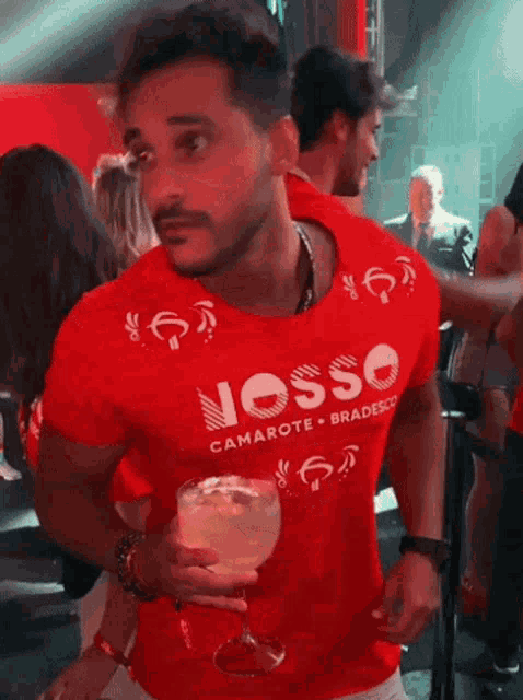 a man in a red shirt that says nosso is holding a glass of wine