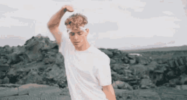 a young man in a white t-shirt is standing in front of a rocky area .