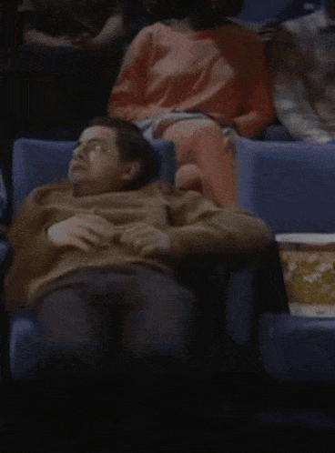a man sits in a theater with a box of popcorn