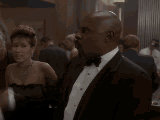 a man in a tuxedo stands in front of a woman in a strapless dress holding money