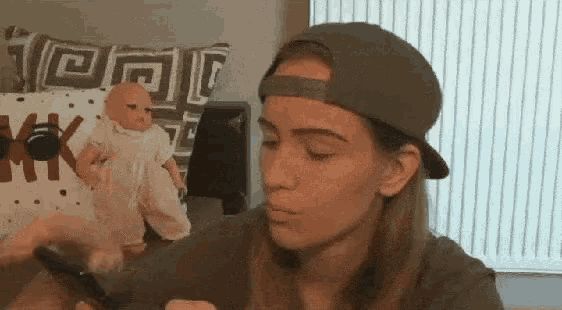 a woman wearing a hat is holding a cell phone in front of a baby doll .