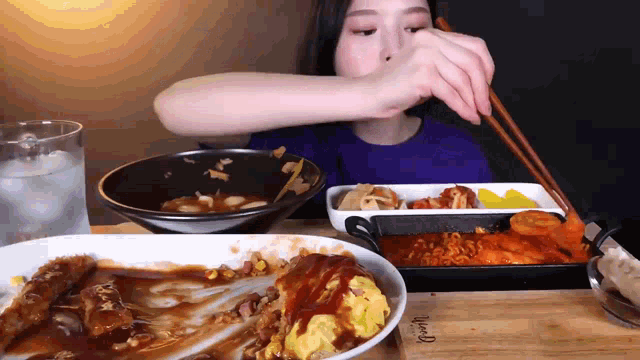 a woman is eating a plate of food with chopsticks and a bowl of soup