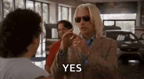 a man wearing sunglasses is talking to another man in a car dealership .