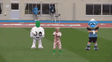 a group of mascots are dancing on a field with a building in the background