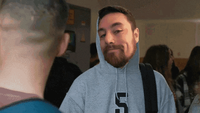 a man with a beard wearing a grey hoodie with the letter u on it