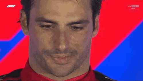 a man in a red and black ferrari jacket is standing in front of a blue and red background .