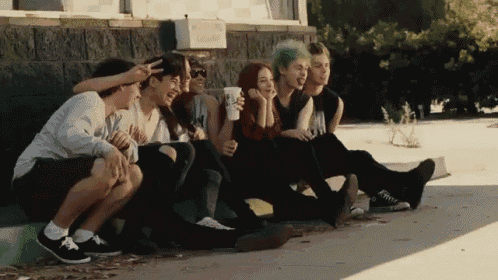 a group of young people are sitting on the sidewalk and one has a green hair color