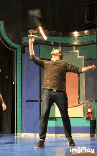 a man stands on a stage with his arms outstretched and a fire extinguisher in the background behind him
