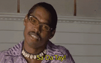 a man wearing glasses , a necklace and a purple shirt is saying sa da tay .