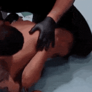 a person wearing black gloves is giving a massage to a man laying on the floor .