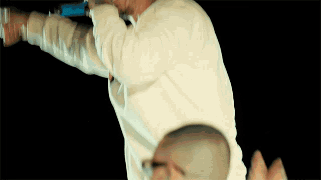 a man in a white sweater is singing into a microphone with his arms outstretched