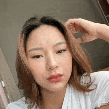 a woman in a white shirt has her hand on her hair