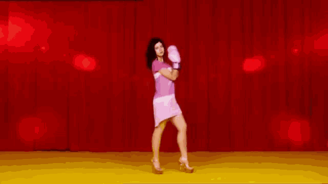 a woman wearing pink boxing gloves is dancing on a stage .