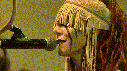 a woman with dreadlocks singing into a microphone with fringe on her head