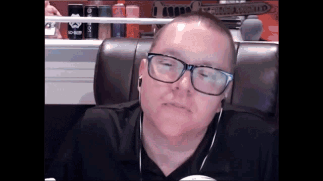 a man wearing glasses and ear buds is sitting in a chair in front of a can that says joker