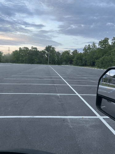 an empty parking lot with trees in the background and a rear view mirror