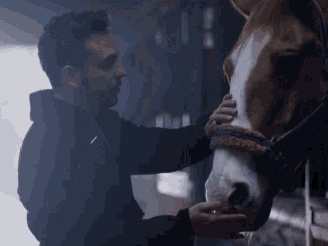 a man petting a brown horse in a dark stable