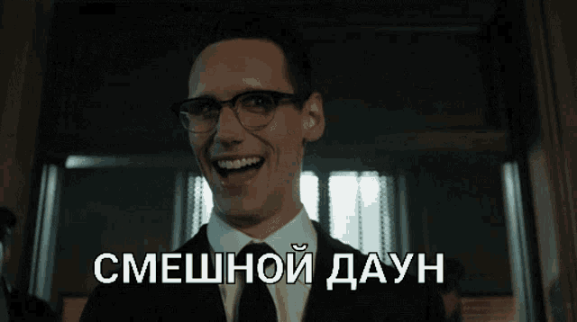 a man in a suit and tie is laughing in a hallway with the words смешной даун written on the bottom right
