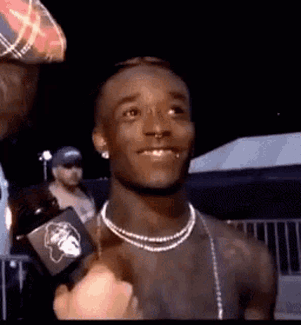 a shirtless man wearing a pearl necklace and earrings is being interviewed by a reporter .