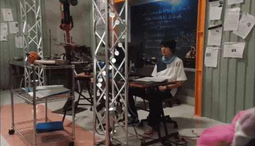 a man sits at a desk in front of a chalkboard that says ' a ' on it