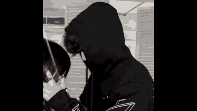 a black and white photo of a man wearing a hoodie and a woman wearing glasses .