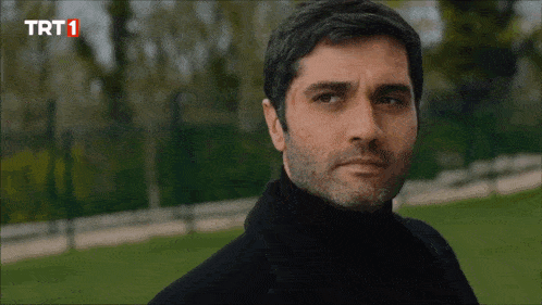 a man in a black turtleneck looks at the camera with trt1 written on the bottom of the screen