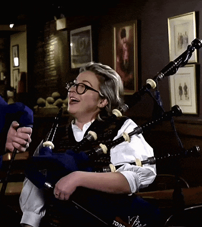 a woman wearing glasses is playing a bagpipe in a room with pictures on the wall