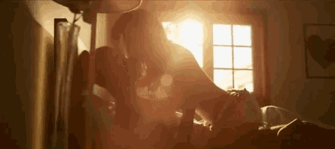 a man and a woman are kissing on a bed while the sun shines through the window .