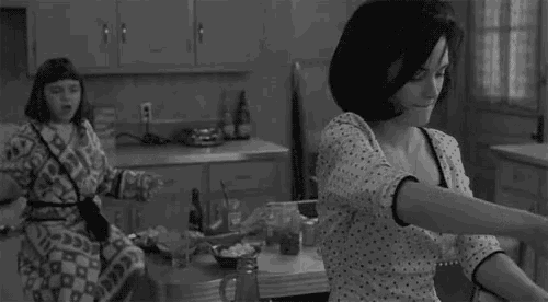 a woman in a polka dot dress is standing in a kitchen with a child .