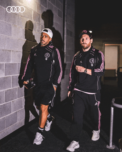 two soccer players are walking down a hallway with an audi logo in the corner